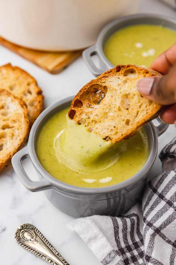 a hand dipping toated ciabatta into soup.