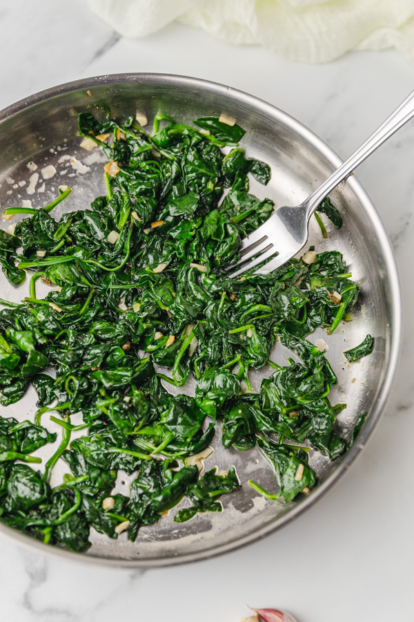 wilted spinach in  skillet with a fork.
