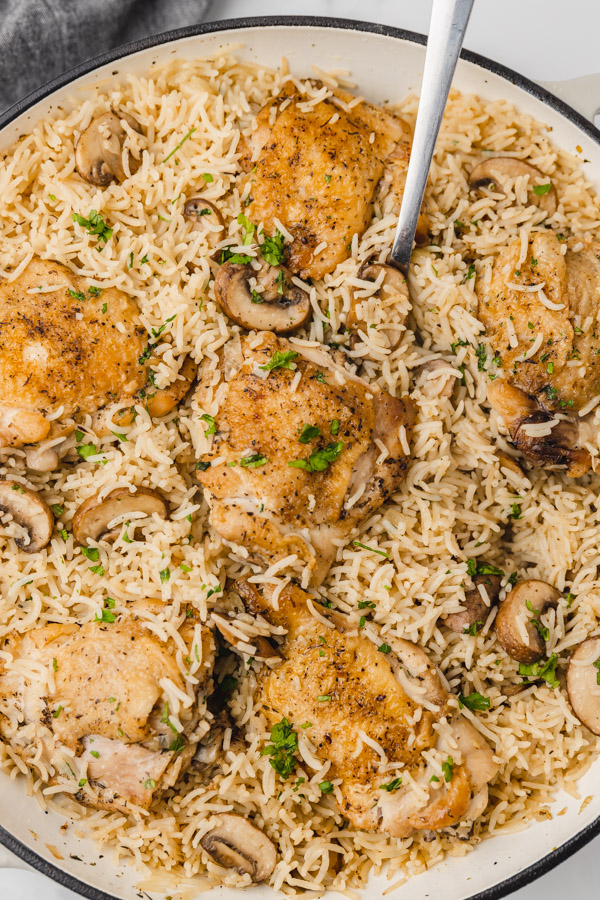 mushroom, rice and chicken thighs in a skillet.