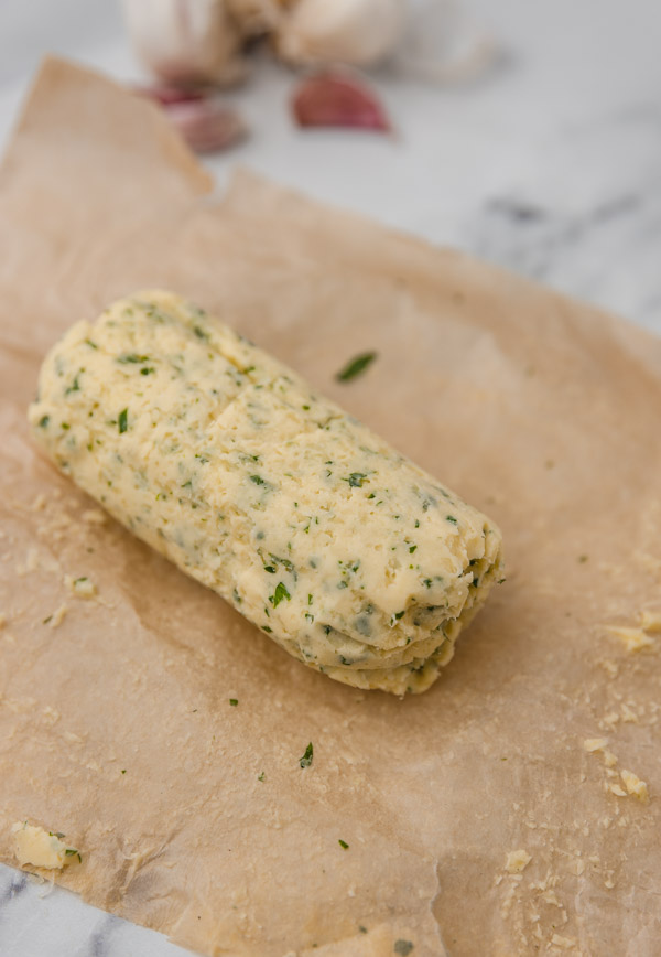 a log of parsley garlic butter on a brown parchment paper.