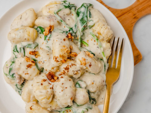 creamy gnocchi with spinach on a plate with a gold fork.