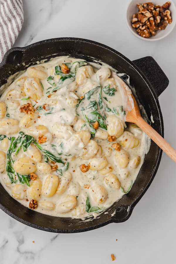 the top view of creamy gnocchi with ladle in a cast iron skillet.