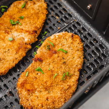 two cooked chicken cutlets in the air fryer basket.