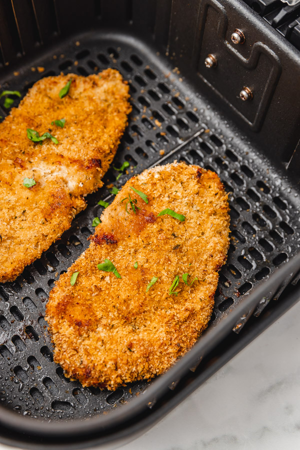 two cooked chicken cutlets in the air fryer basket.
