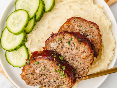 a plate of mashed potatoes and meatloaf and cucumber salad.