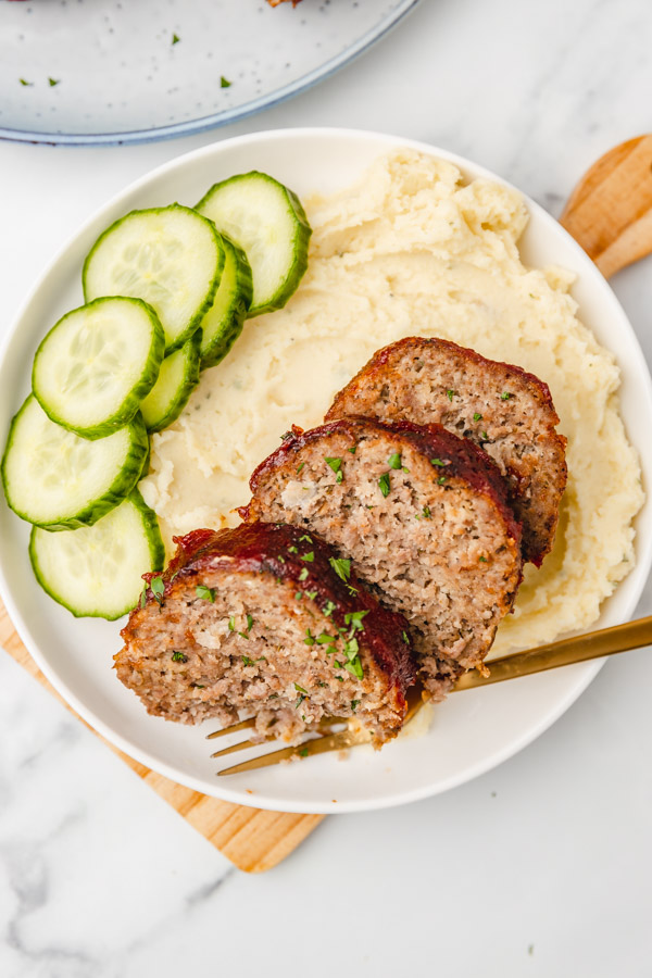 overhead shot of a plate of three slices of meatloaves placed on mashed potatoes.