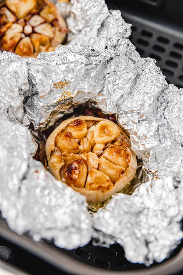 two roasted garlic in an aluminum foil in an air fryer basket.