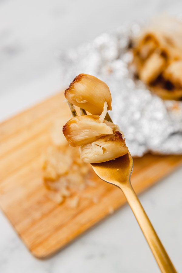 three roasted garlic cloves on a golden fork.