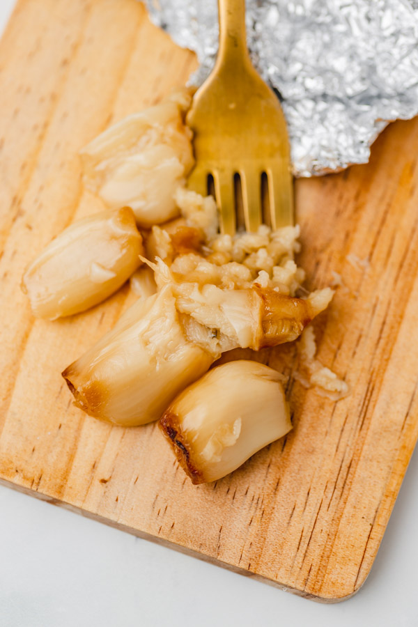 a fork mashing roasted garlic on a board.