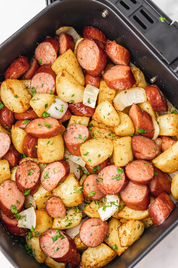 cooked potatoes, sausages and onion in an air fryer basket.