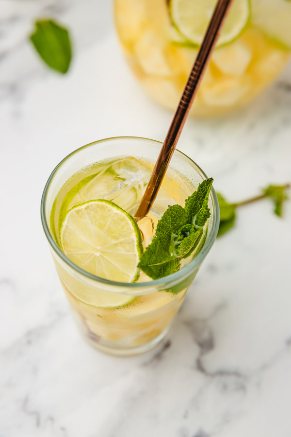 a glass of pineapple water with mint leaves and a slice of lime with a straw.