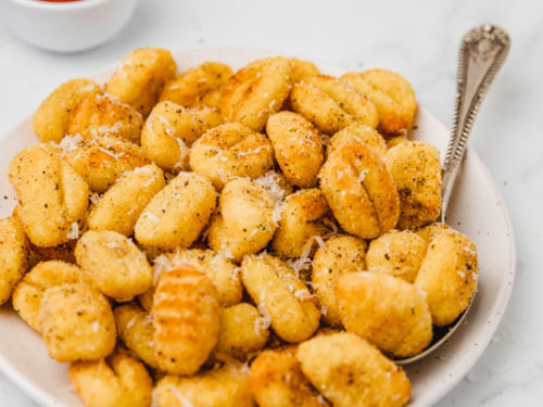 a plate of crispy air fried gnocchi placed beside a small tub of marinara sauce.