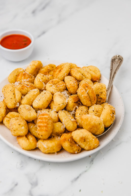 a plate of crispy air fried gnocchi placed beside a small tub of marinara sauce.