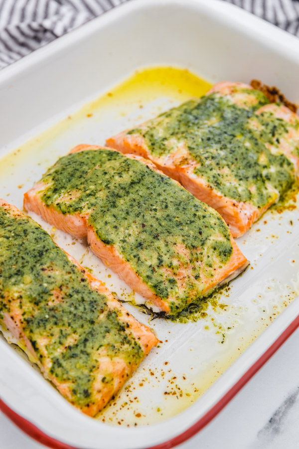 three freshly baked salmon covered with pesto resting in a baking sheet.