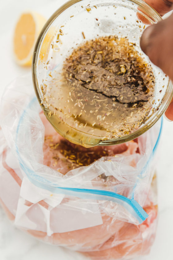 a hand pouring marinade over chicken in a freezer bag.