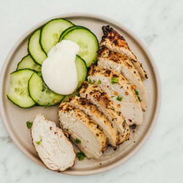 sliced chicken breast with a side of cucumber salad on a beige plate.
