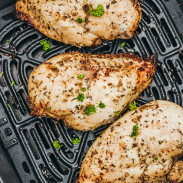 three cooked chicken breast in an air fryer basket.