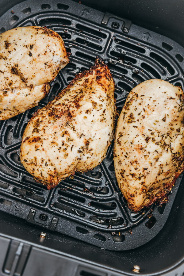 three cooked whole chicken breast in an air fryer basket.