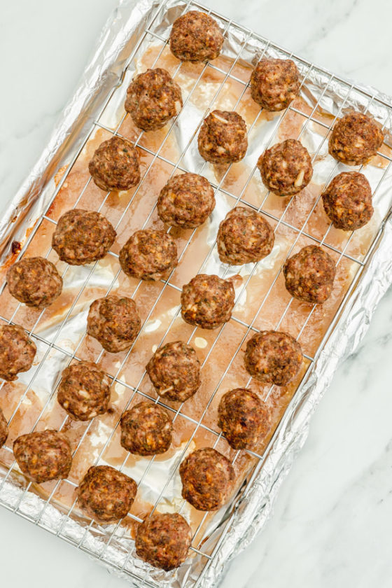 freshlt baked meatballs on a wire rack with the dripping sitting on the lined baking sheet.