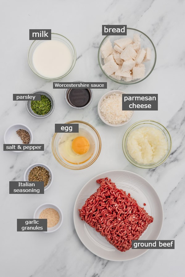 ingredients to make meatballs placed on a white marble surface.