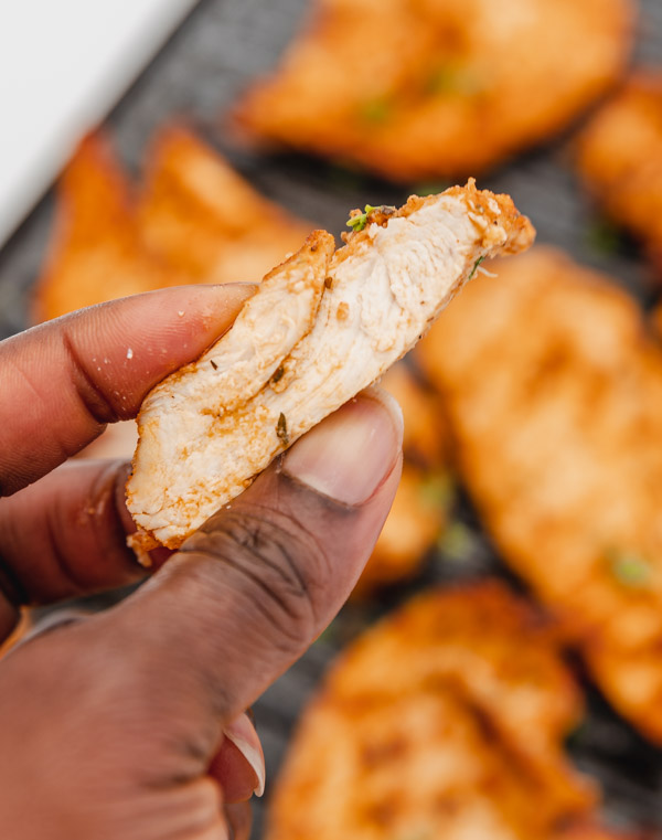 a hand hold sliced chicken showing how juicy and tender the inside is.