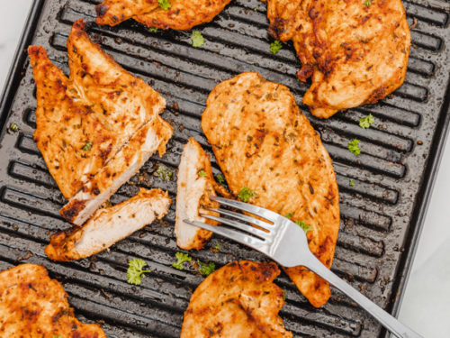 six cooked chicken on a griddle pan with one of the chicken already sliced.