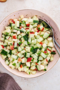 cucumber apple salad in a pink bowl with two spoons.
