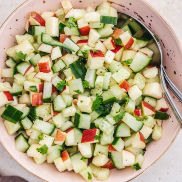 cucumber apple salad in a pink bowl with two spoons.