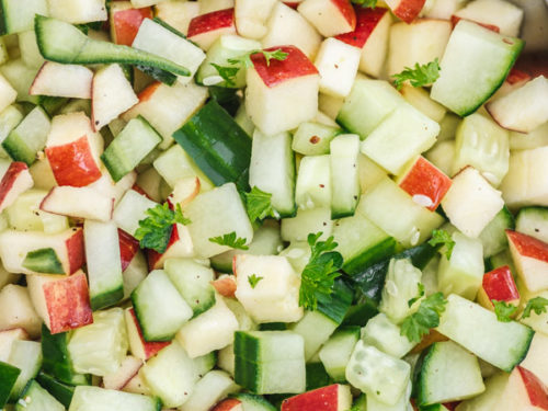 a close up of cucumber and apple salad in a pink bowl.