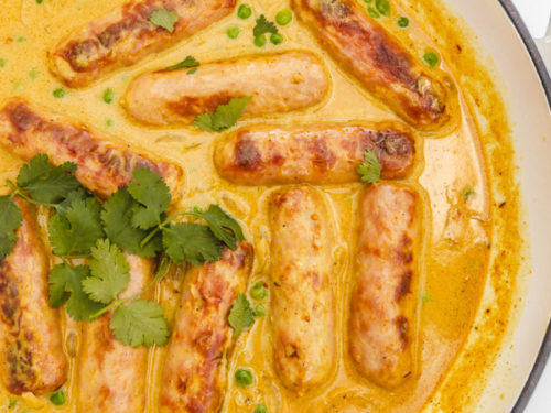 a skillet of freshly cooked curied sausages garnished with fresh cilantro leaves.