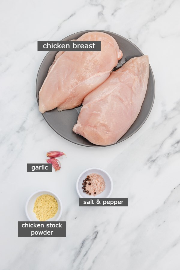 ingredients needed to make boiled chicken breasts laid on a marble surface.