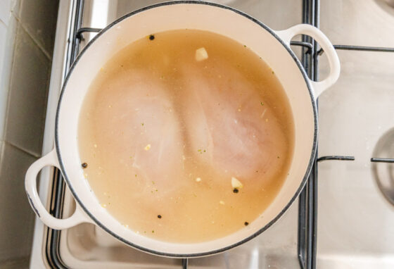 a pot containing two boneless chicken breasts covered with water placed on a gas cooker.