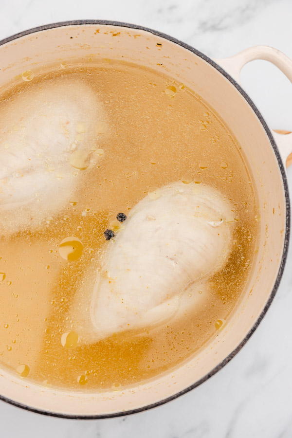 cooked boiled chicken breast in a pot sitting in its broth.