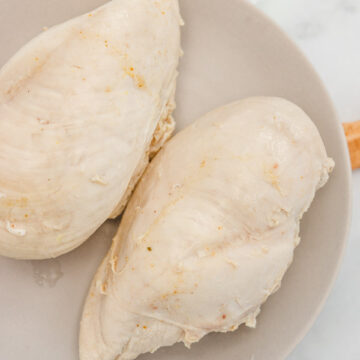 two whole boiled chicken breasts on a plate.