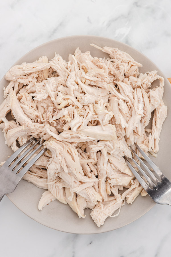 shredded chicken breast on a plate with two forks placed on each side of the plate.