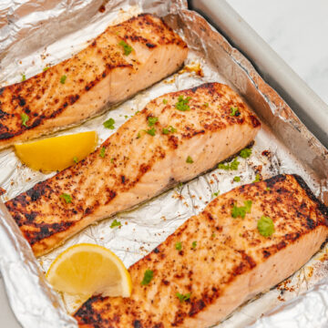 three broiled salmon in a foil lined baking sheet.