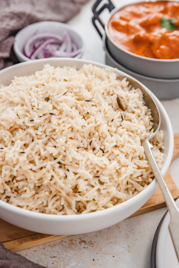 a close shot of a bowl of jeera rice placed on a wooden board with a big serving spoon.