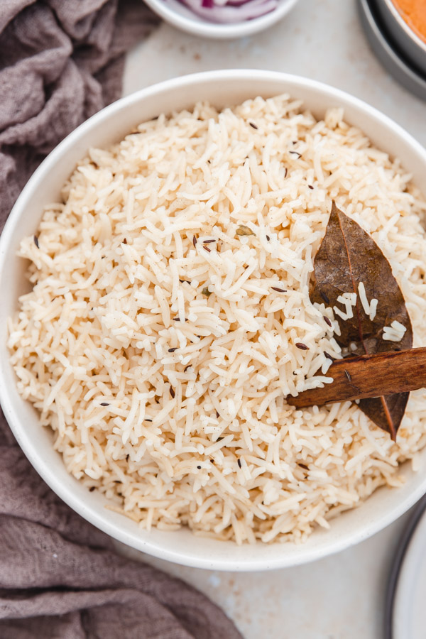 a bowl of jeera rice garnished with a bay leaf and one cinnamon stick placed beside a brown napkin.