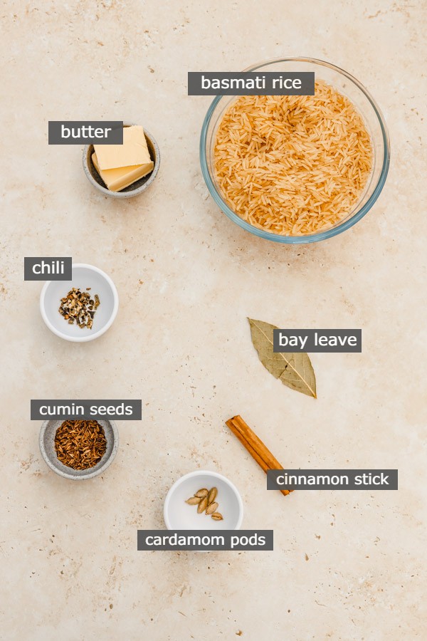 the ingredients needed to make cumin rice laid on a brown surface.