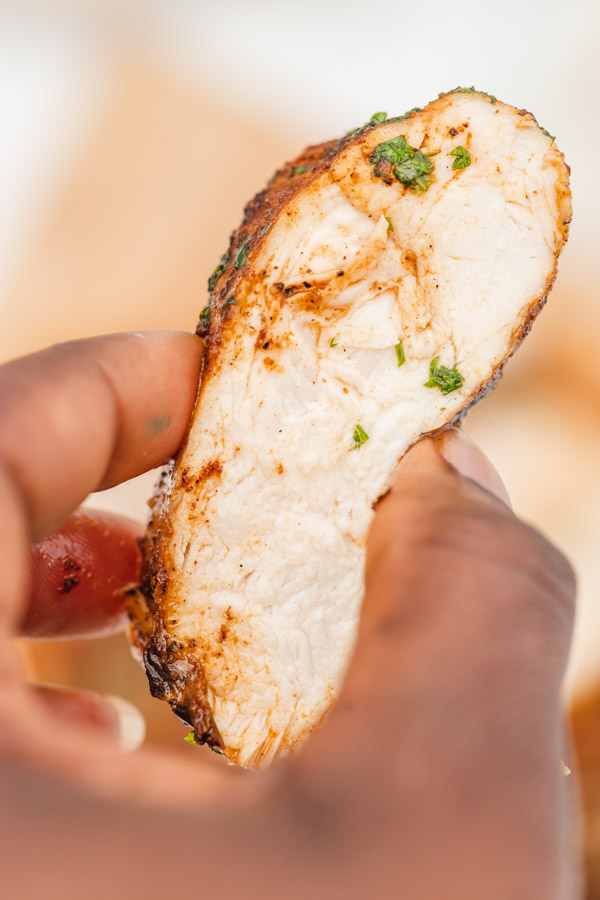 a hand holding up a piece of sliced juicy chicken breast. 