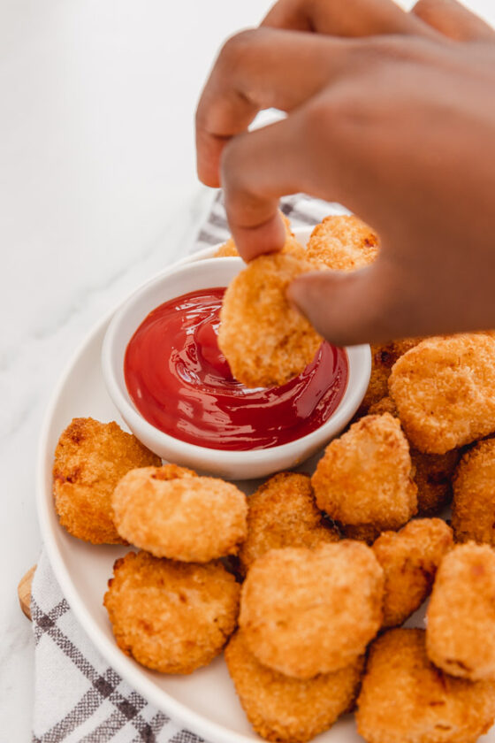 a hand dipping a chicken nugget into ketchup.