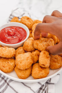 a hand reaching for chicken nugget on a plate.