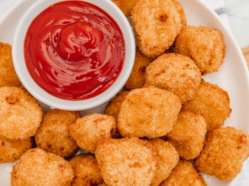 chicken nuggets on a plate with a pot of ketchup.