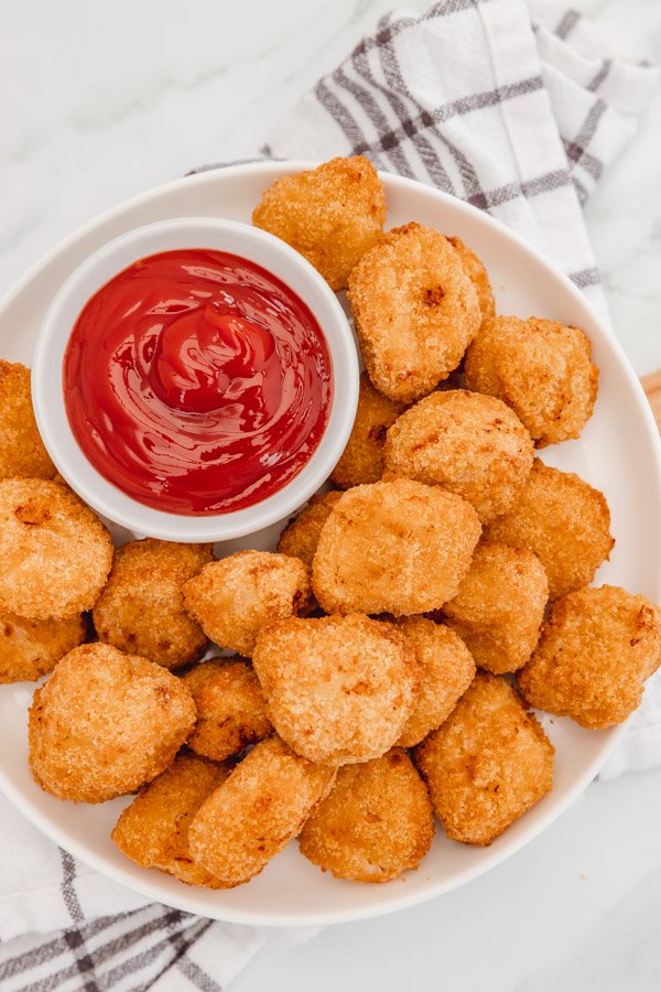 chicken nuggets on a plate with a pot of ketchup.