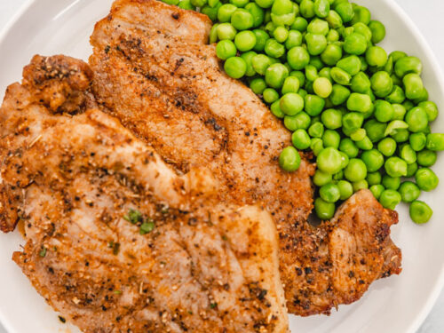 a plate of pork steak and green peas with butter dipping sauce on the side.
