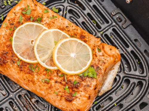 cooked salmon side garnished with three lemon slices in an air fryer basket.