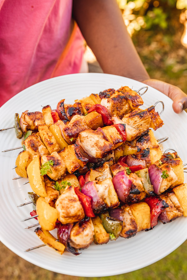a hand holding up a plate of chicken kabobs.