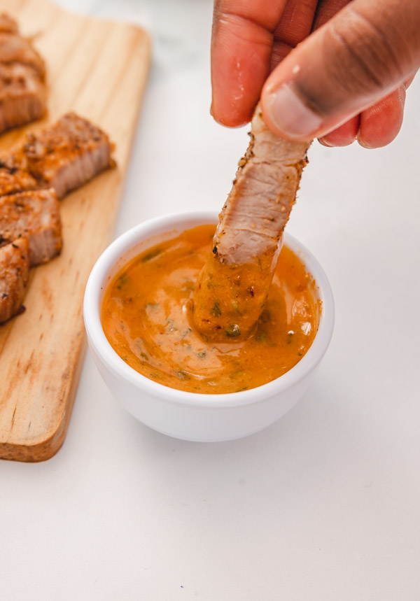a hand dipping sliced steak in cowboy dipping sauce.