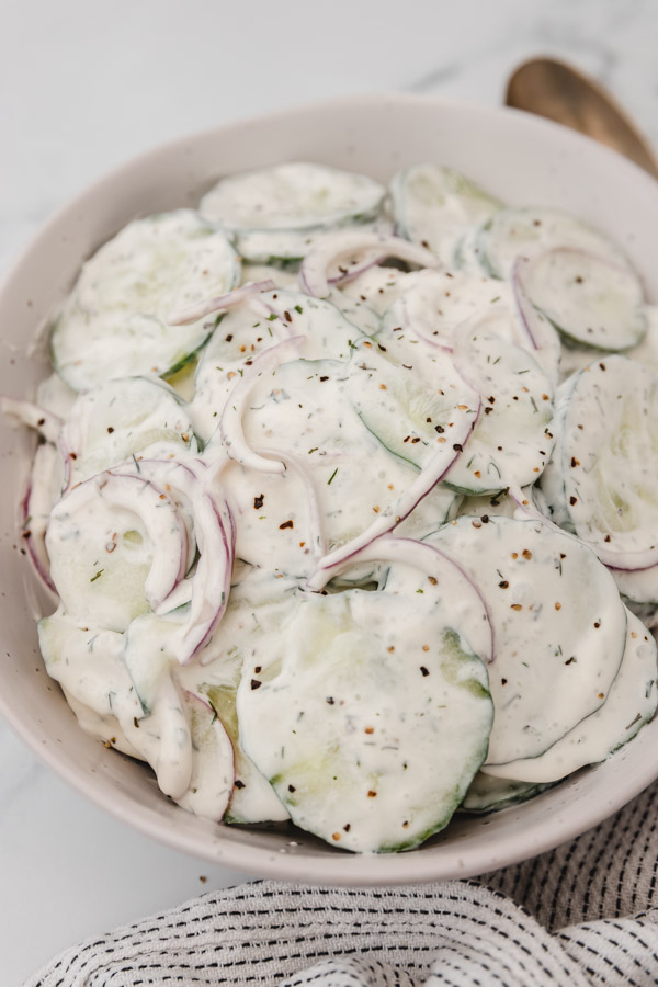 creamy cucumber salad with onions in a bowl placed beside a napkin.