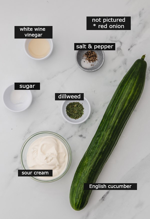ingredients to make cucumber salad on a white marble surface.